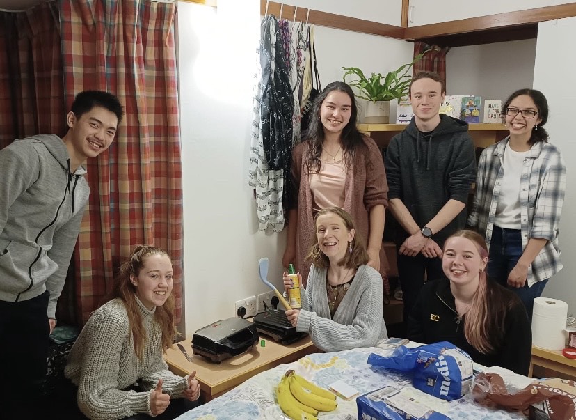 A group of people in a room smiling. They are cooking.